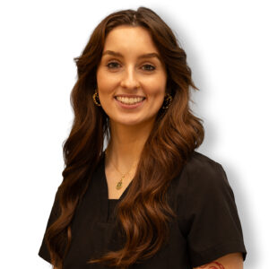 Sarah Neky, a healthcare professional with long brown hair, wearing black scrubs and gold jewelry, smiling against a white background.